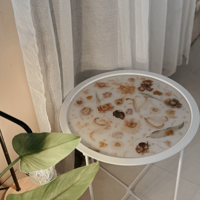 Round side table with a preserved-flower resin top, viewed from above beside a plant