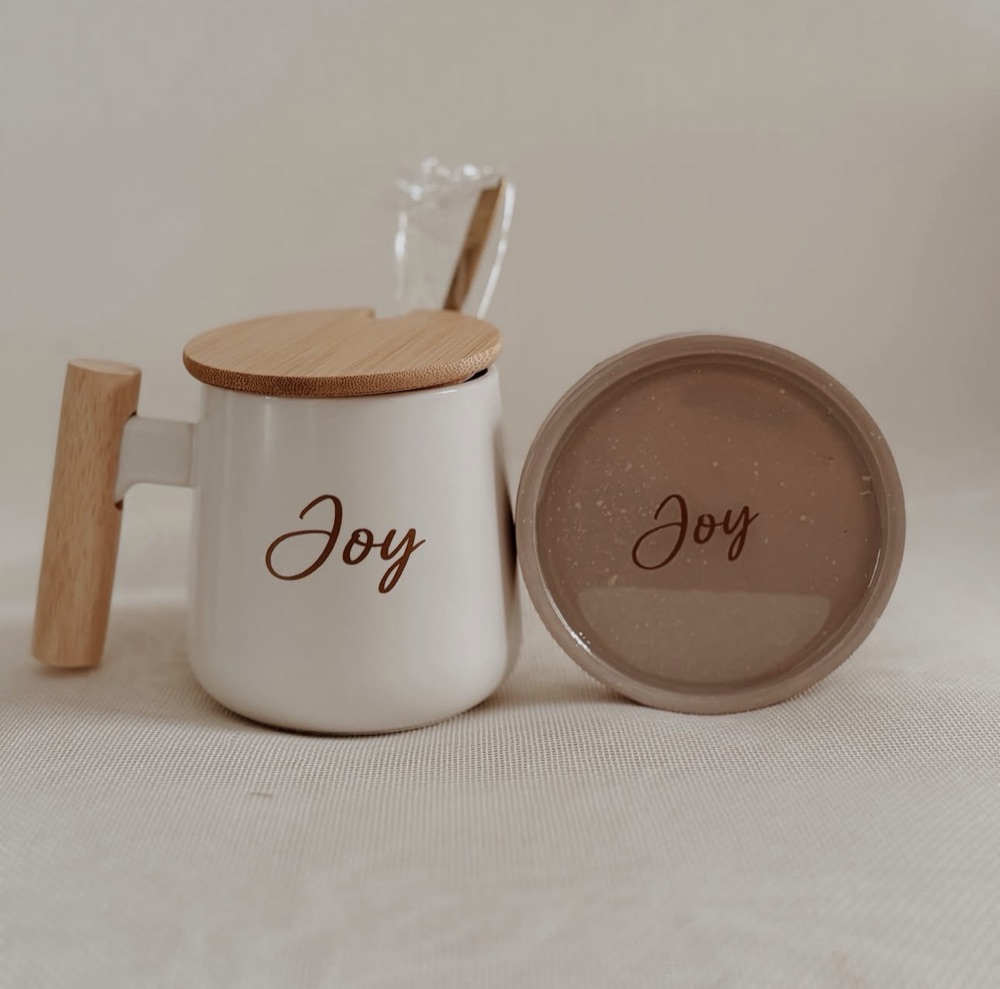 White Nordic mug with wooden handle and bamboo lid, personalized with the name Joy, beside a matching speckled cement and resin coaster