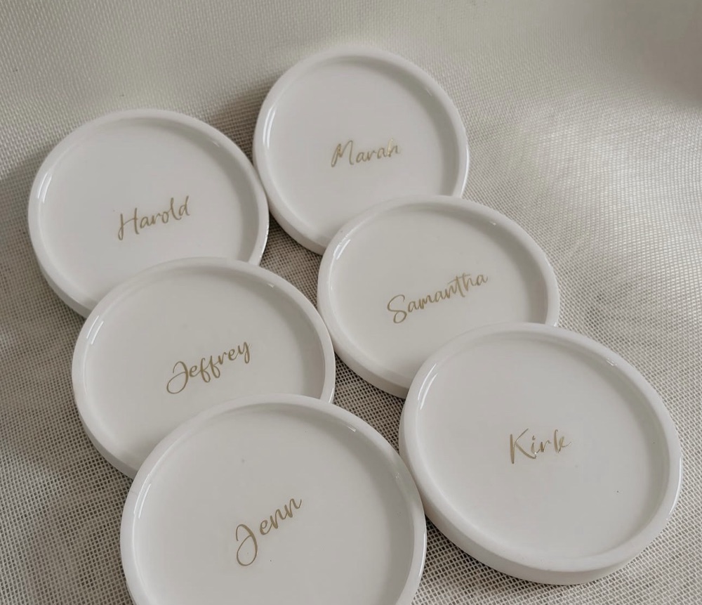 Glossy white round coasters, each personalized with a guest's name in gold script